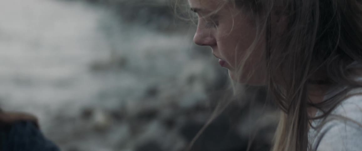 Woman rolls a cigarette sitting next to water