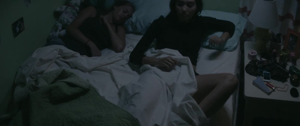 Two women lay in bed at night and one sits up and opens a nightstand drawer