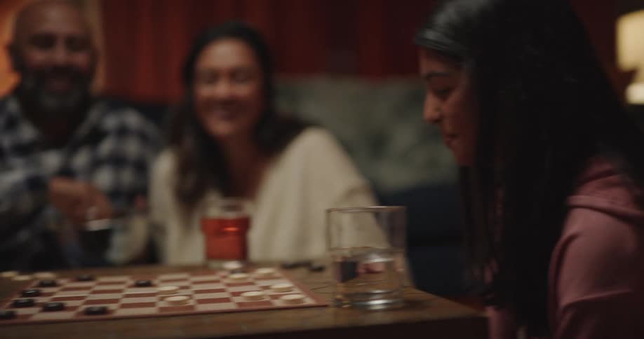 A teenage girl and her brother plays checkers and the boy celebrate with a high five with his father while their parents watches from the background in a cozy home setting