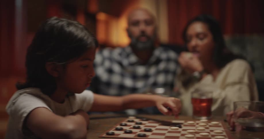 Family members play a board game together around a table in a warm cozy living room