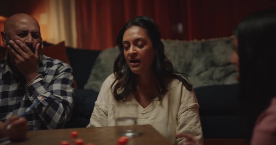 A family of four sit around a table in a living room happily playing a dice game