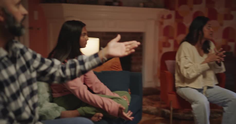 A woman gestures enthusiastically at a child standing from an armchair as others react around her in a cozy retrostyled living room during a lively group moment