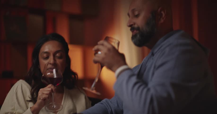 A couple enjoys a cozy evening at home relaxing on the couch while talking and drinking red wine