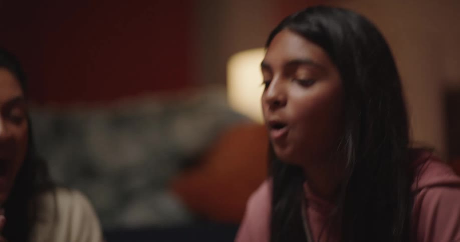 A teen girl rolls dice on a table and then high fives two seated people in a living room