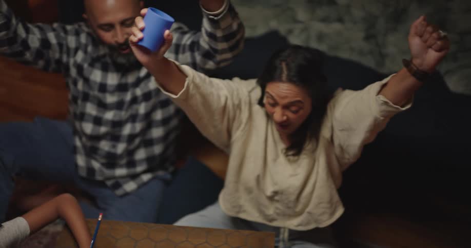 Woman playing dice at a dice game table accompanied by another adult and children having fun