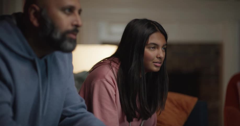 A daughter jumps up in excitement while playing a video game with her father