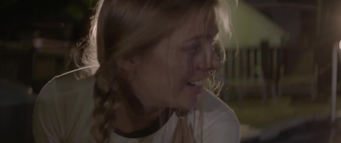 A woman looks to the side and smiles outside at night