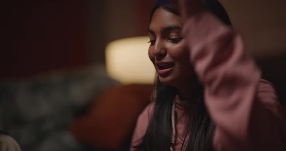 A young woman excitedly rolls dice from a cup while playing a board game with her family in a warmly lit room