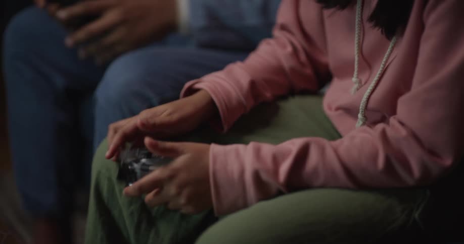 A man and a teenage girl sit on a livingroom couch playing a video game with a table in front of them covered in snacks
