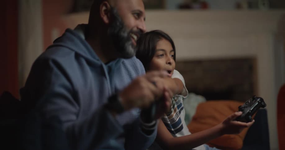 Father and daughter playing a video game with controllers while sitting in a living room
