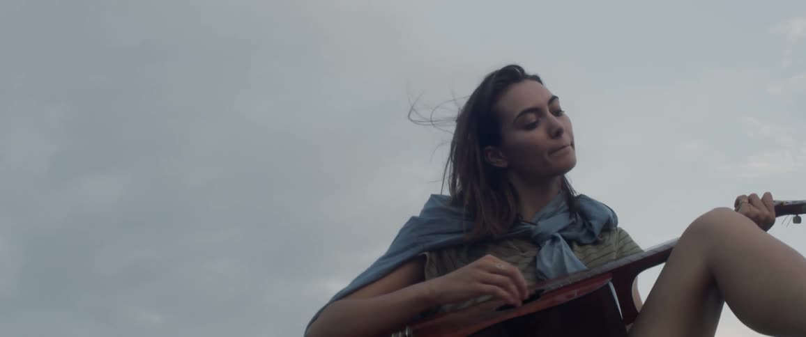 A woman sits outside on a cloudy day playing guitar