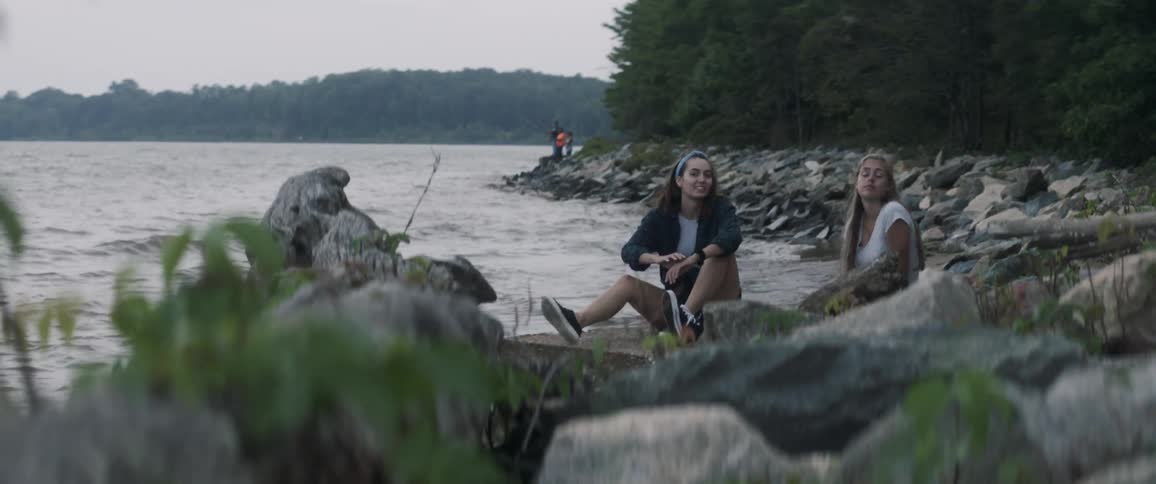 Two girls sit on the bank of a river