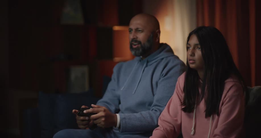 Father snacks and plays a video game with his daughter at home during the evening