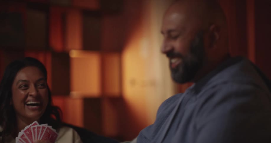 A woman concentrates intensely on her hand of cards while playing a game with a man in a cozy dimly lit room her expression shifts from focused determination to joyful laughter as the couple shares a lighthearted and competitive moment together