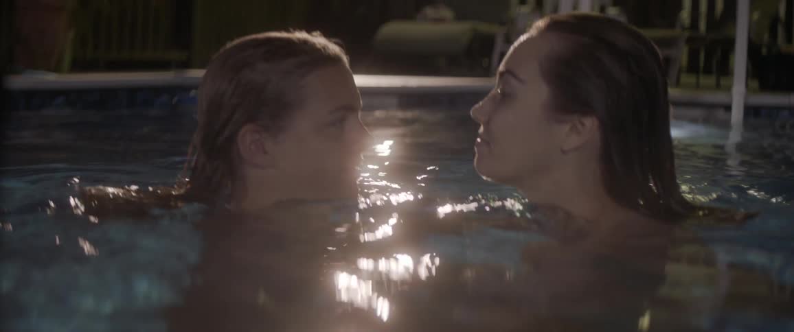 Two girls swim around each other in a pool at night