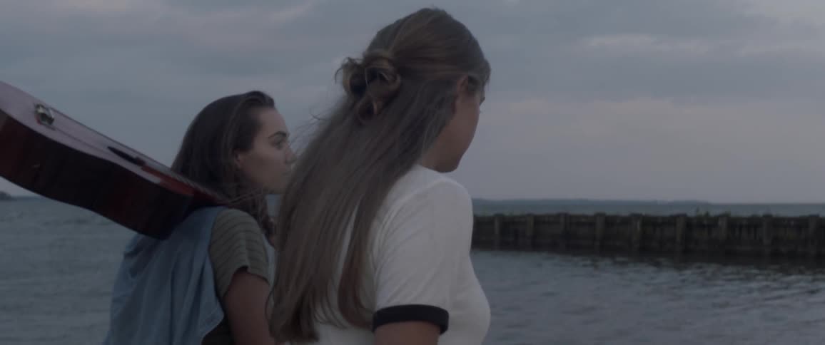 Two women walk near the ocean with a guitar