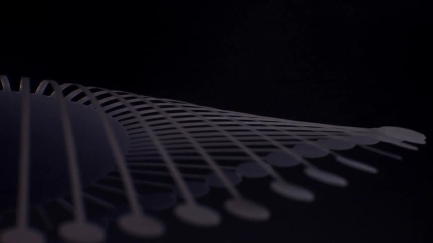 A darktoned kinetic sculpture composed of numerous slender rods with circular tips rotates in a fluid wavelike motion against a black backdrop