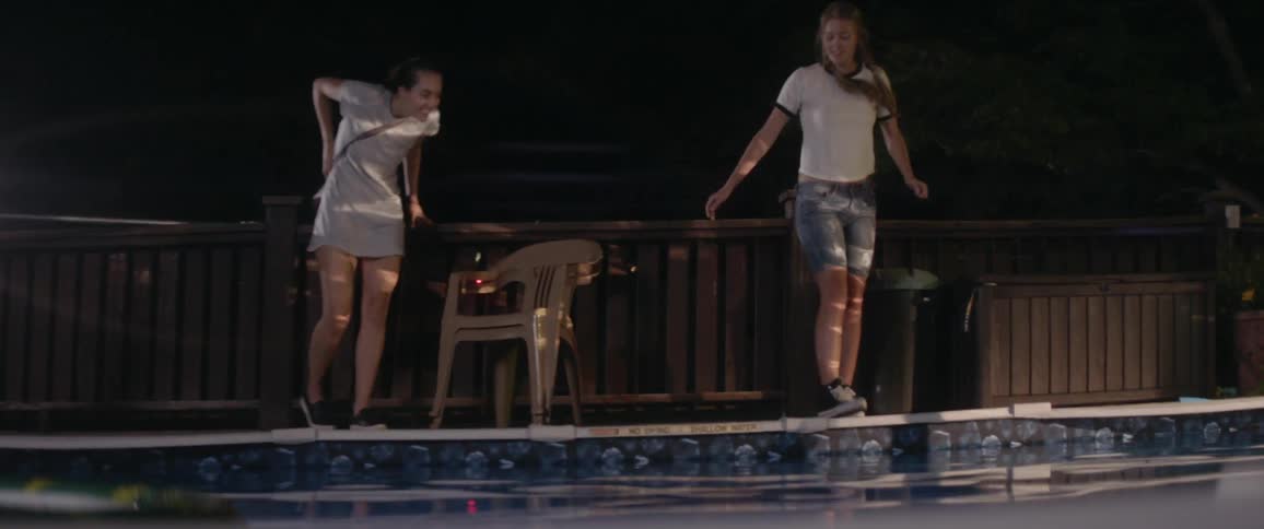 Two women climb over a fence to access a swimming pool