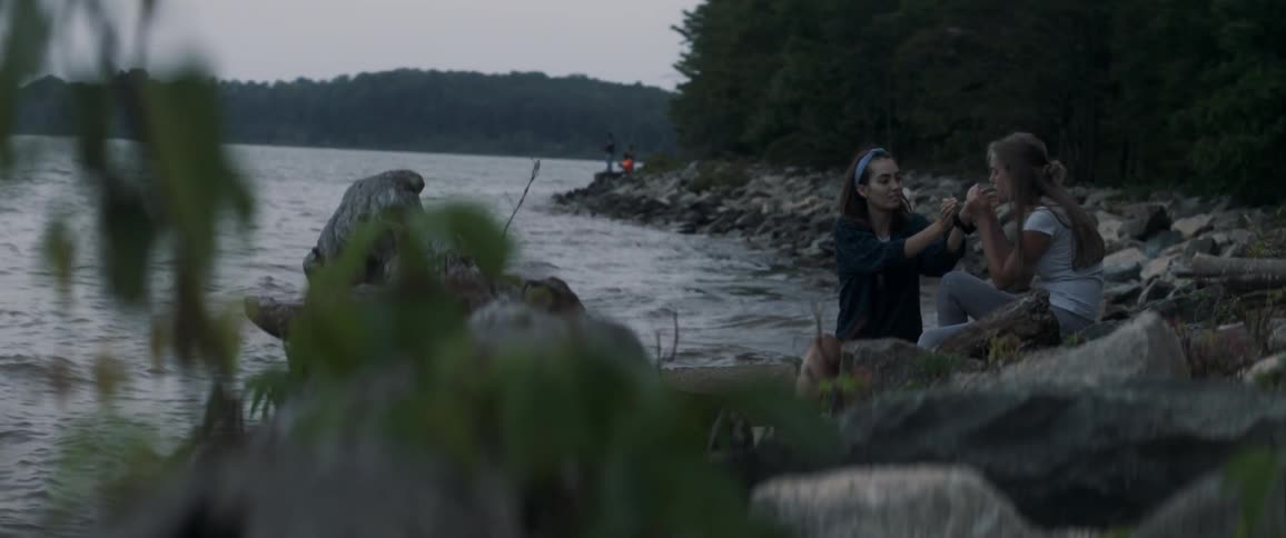 Two women sit on a rocky beach