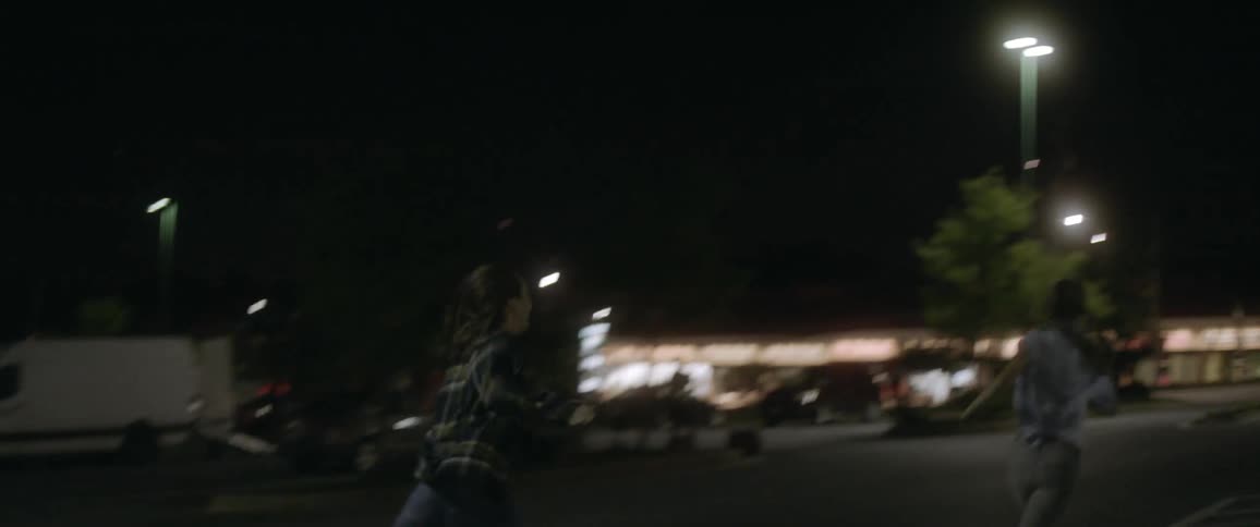 Two women running down a parking lot at night
