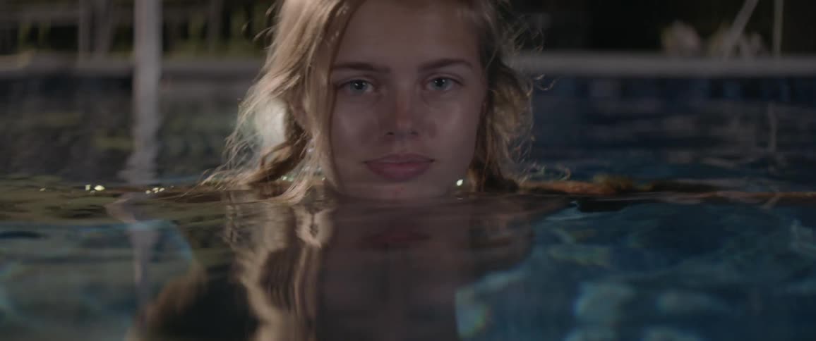 Smiling woman stands in a swimming pool at night