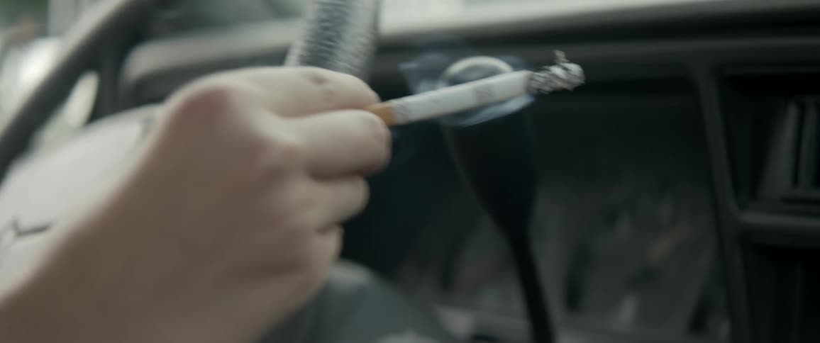 A person holds a burning cigarette while driving a car