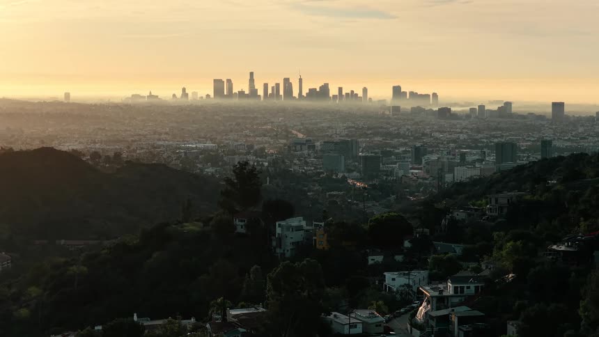 Residential neighborhood occupies a hill on the outskirts of a city while the skyline contrasts with the red sky