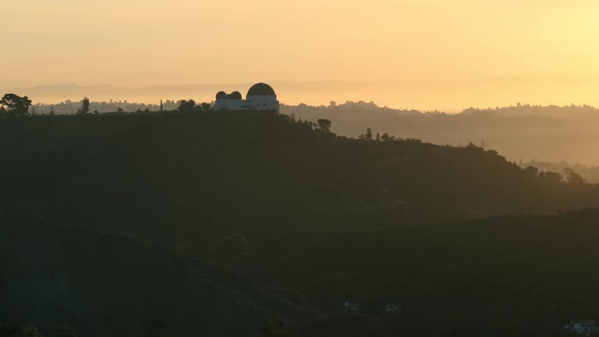 A building sits atop a hill in the countryside surrounded by grass and glowing in the warm light of sunrise