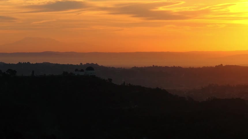 Trees on mountains across the landscape under a colorful cloudy sunset sky
