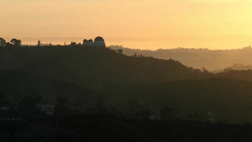 A building sits atop a hill in the countryside surrounded by grass and glowing in the warm light of sunrise