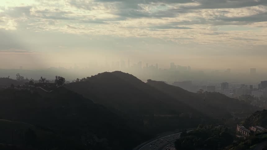 Winding highway through wooded hills with hazy cityscape in the background