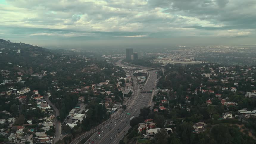 The multilane highway the 405 freeway creates a sweeping diagonal grey line that leads the eye from the bottom of the frame toward the twin towers in the distancethe layer of smog and lowhanging clouds forms a hazy horizontal line across the midd