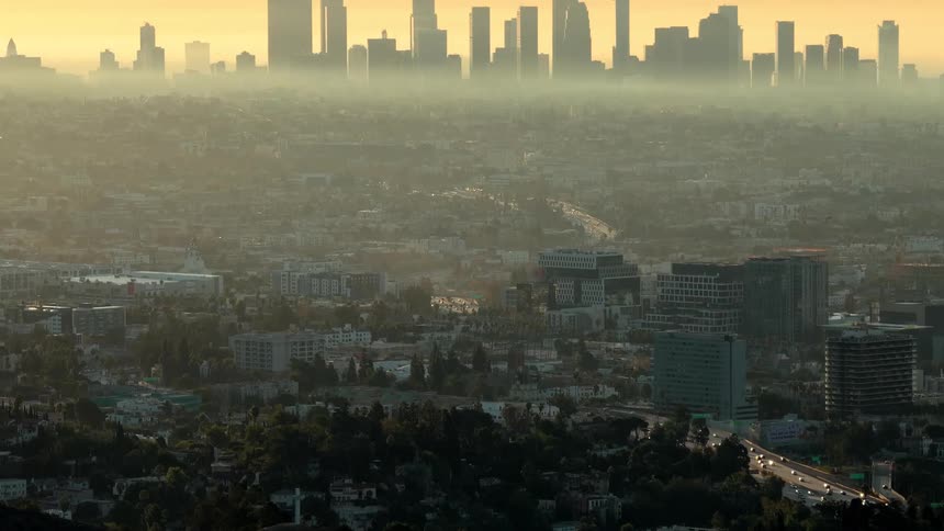 The sun is rising through the clouds over a city in a valley
