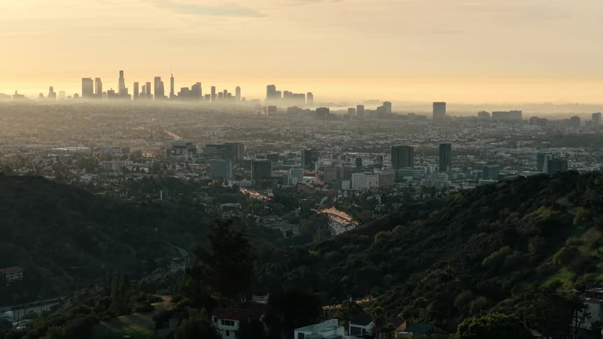 Green hills with winding roads leading to downtown los angeles under a golden hazy sky