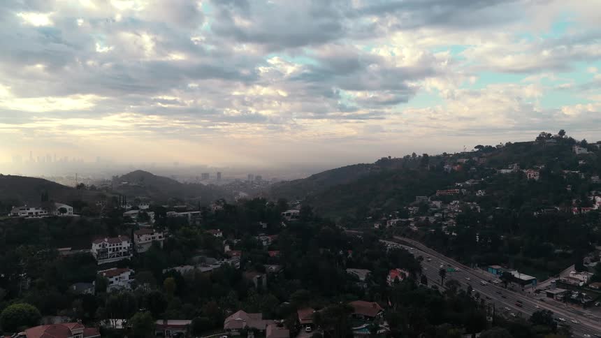 Aerial view of a hillside residential area with a winding highway and a partly cloudy sky