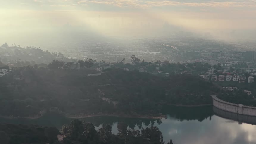 Reservoir bordered by greenery and urban areas with hazy cityscape in the background