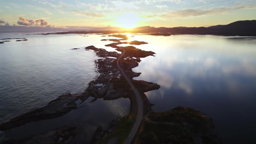 A stunning aerial shot glides over a scenic highway that connects a series of rocky islands as the setting sun casts a golden glow across the ocean