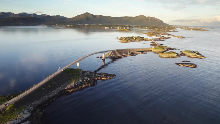 Cars travel on a road with a bridge connecting islands with houses and mountains along the coast