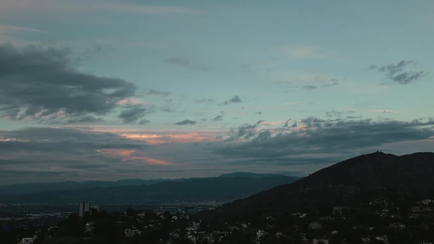 A wide serene view shows a vast cloudfilled sky with hints of a fading sunset glowing above rolling mountains and a sprawling cityscape below