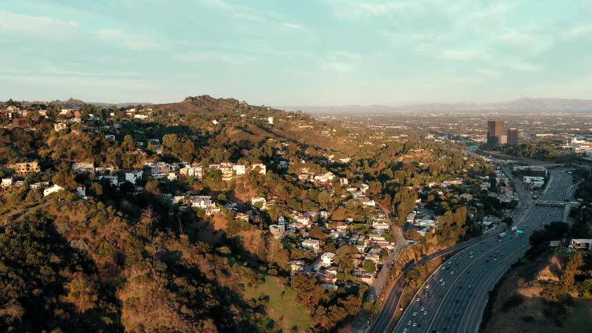 The iconic hollywood sign sits on the rugged brushcovered slopes of mount lee beneath a cloudy overcast sky a tall communications tower stands on the peak directly above the famous white lettering as the camera pans across the hillside