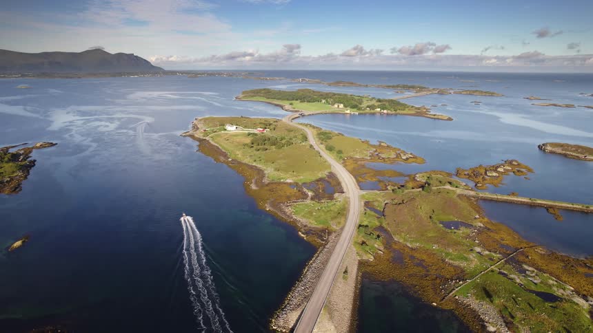 Car travels on a road with bridges connecting islands with houses as a boat sails on the water with mountains along the coast