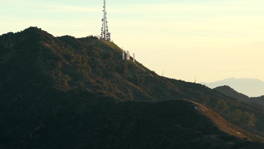 A cell tower stands at the top of a hill in the countryside silhouetted against the warm colors of sunset