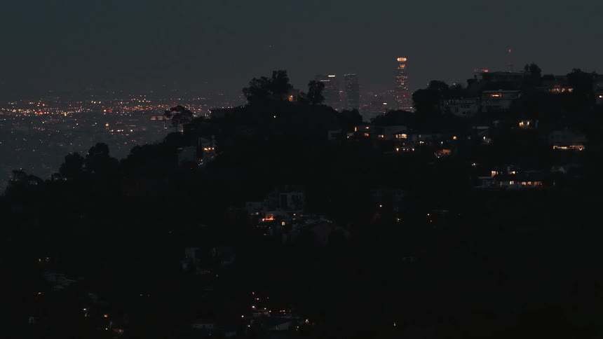 Nighttime urban landscape with lit hillside homes and skyscrapers in the background