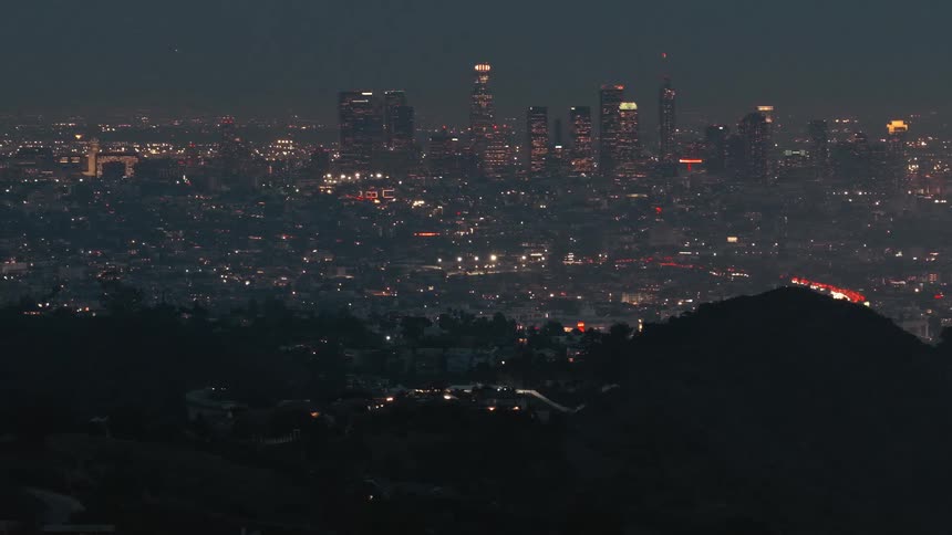 View of a city from over the edge of a mountain as lights on towers and skyscrapers glow on the skyline