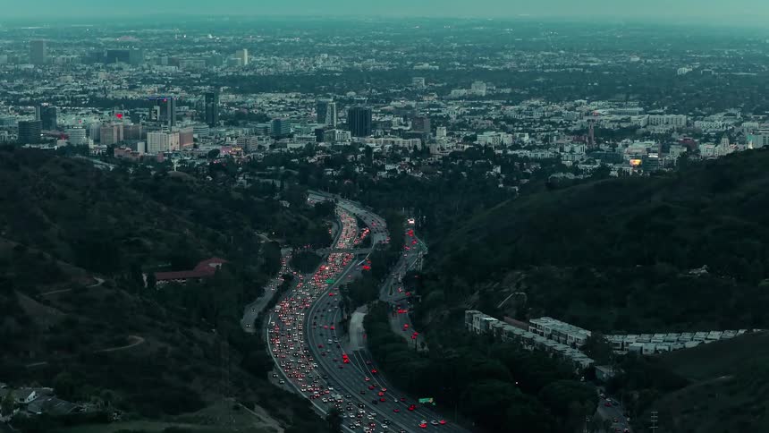 Aerial of moving cars on a city highway with distant buildings at dawn