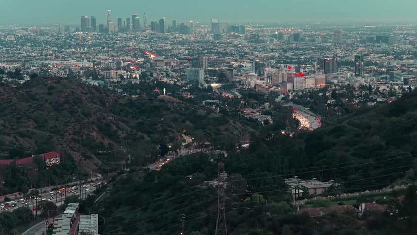 Metropolitan area next to hills covered in trees divided by a road outdoors during day time