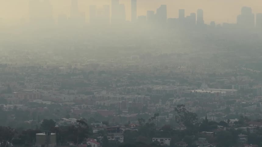 A city skyline emerges through a foggy atmosphere at sunrise softly glowing in the early light