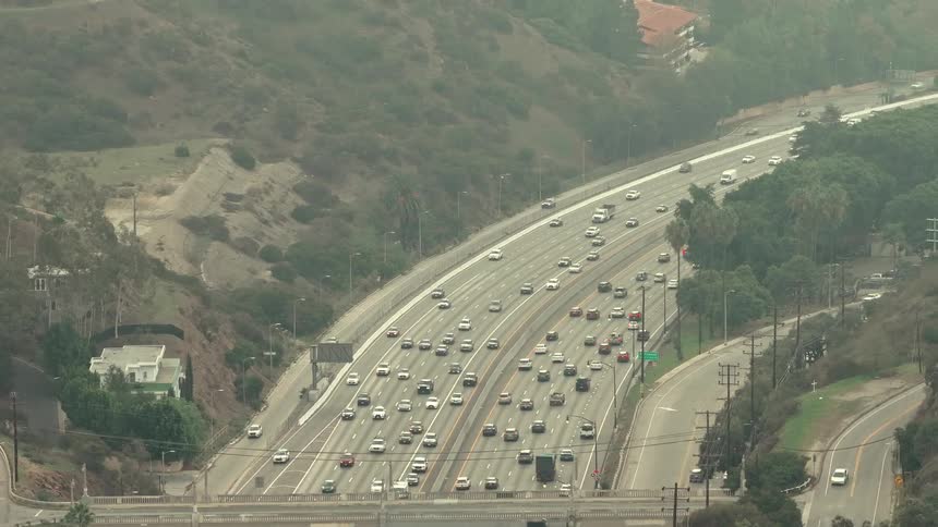 He sweeping horizontal line of the multilane highway that stretches across the landscape filled with moving trafficthe soft undulating line of the mountain ridge in the background that separates the residential hills from the hazy horizon