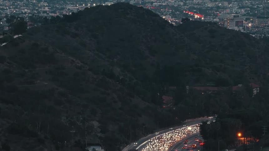 Aerial view of automobiles moving in many lanes stuck in heavy traffic on the highway in a crowded city with towers and buildings on the city skyline