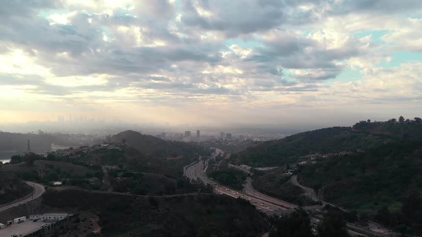 Urban area nestled in wooded hills with winding highway and city skyline in the distance